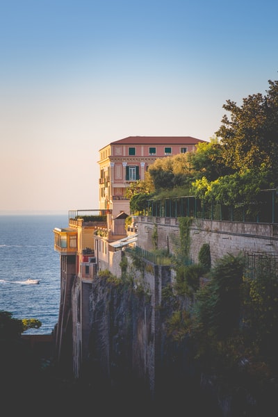 On the cliff pink concrete house, during the day can see the blue sea
